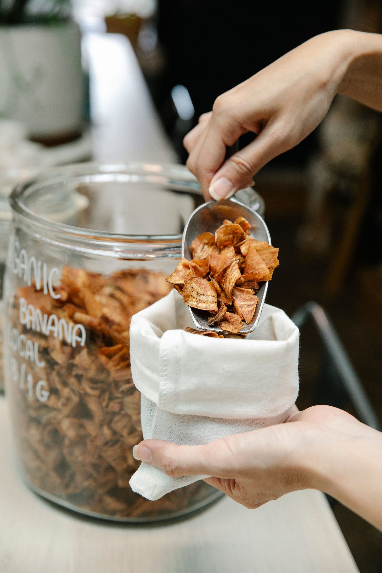 Hands scooping dried banana chips into a cloth bag