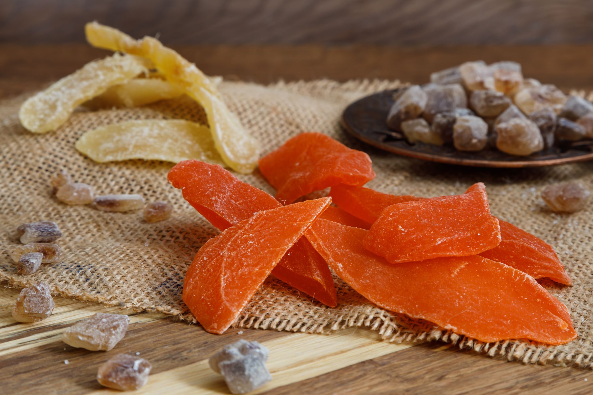 Soft-dried mango slices on burlap with candied fruit behind