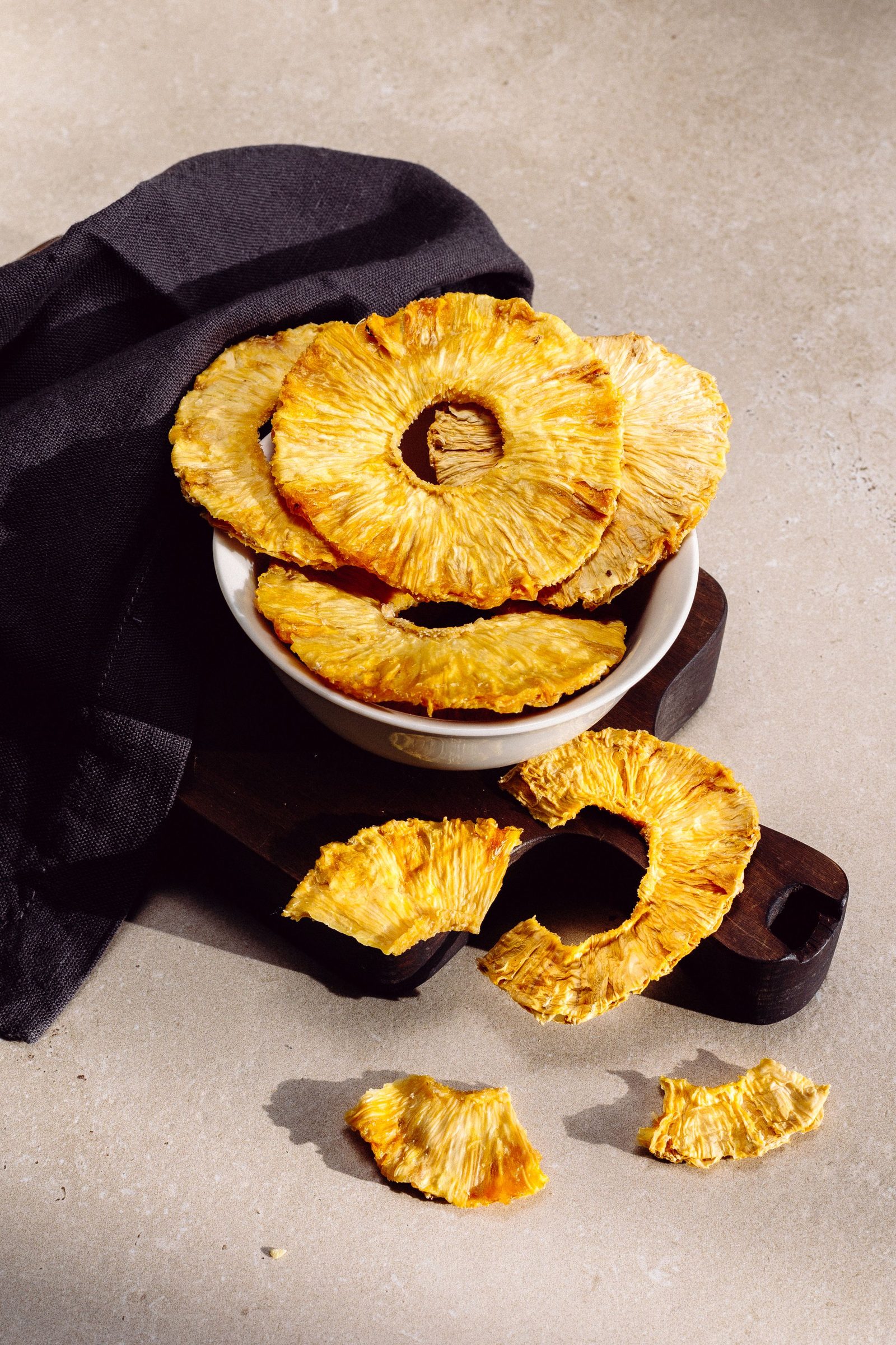Golden dried pineapple rings in a bowl on dark linen